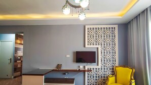 Een moderne woonkamer met een bureau, een televisie, een decoratief wandpaneel, een gele fauteuil en een blauwe bank.