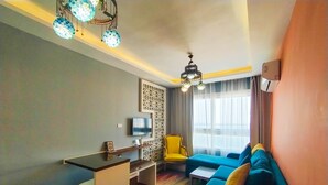 Een moderne woonkamer met een blauwe bank, een klein tafeltje, een televisie en decoratieve verlichting.