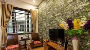 A cozy room with a wooden TV stand, a small table, and a cushioned bench. - Dollar Homestay & Travel (Hanoi)