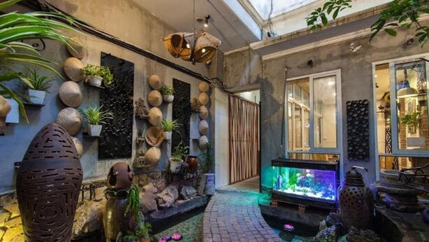 A narrow indoor garden with a water feature, stone sculptures, and various potted plants. - Dollar Homestay & Travel (Hanoi)
