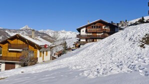 A wooden chalet with a balcony, set against a snowy mountain backdrop.
