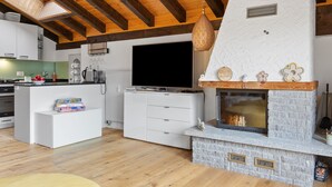 A modern kitchen with a TV, white cabinets, and a stone fireplace.
