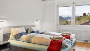 A modern bedroom with a large bed, a nightstand, and a window with a mountain view.