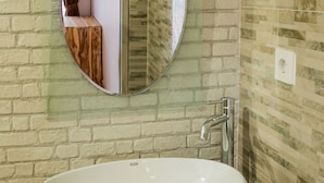 A bathroom with a large oval sink, a round mirror, and a brick wall. - Kayu Kuning Cottage (Penida Island)