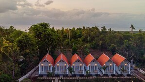 A row of white buildings with red roofs, surrounded by lush greenery and a view of the ocean. - Kayu Kuning Cottage (Penida Island)