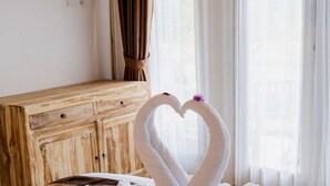 A hotel room with a bed, a wooden dresser, and a window with curtains. - Kayu Kuning Cottage (Penida Island)