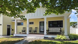 Een tweelaags huis met een veranda, nummer 208, met een bank, stoelen en een kleine tuin.