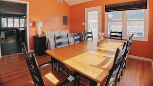 Een eetruimte met een houten tafel en stoelen, een plafondventilator en uitzicht naar buiten door een raam.
