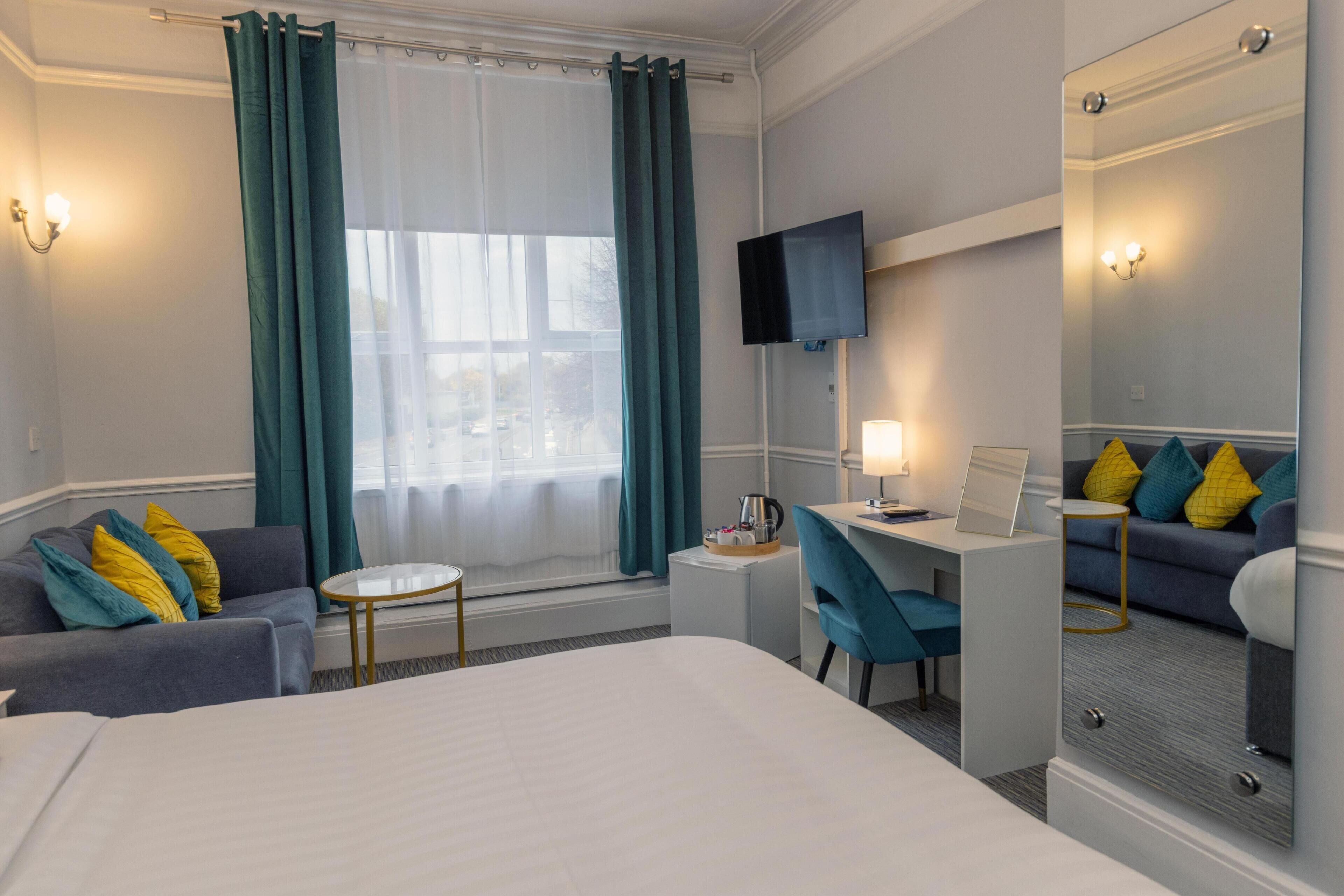 Une chambre d’hôtel avec un lit, un bureau, une chaise, une télévision et une fenêtre avec des rideaux.