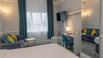 Une chambre d’hôtel avec un lit, un bureau, une chaise, une télévision et une fenêtre avec des rideaux.