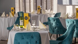 Een eethoek met smaragdgroene bekleden stoelen, witte tafelkleden en netjes gedekte tafels met wijnglazen en menukaarten.