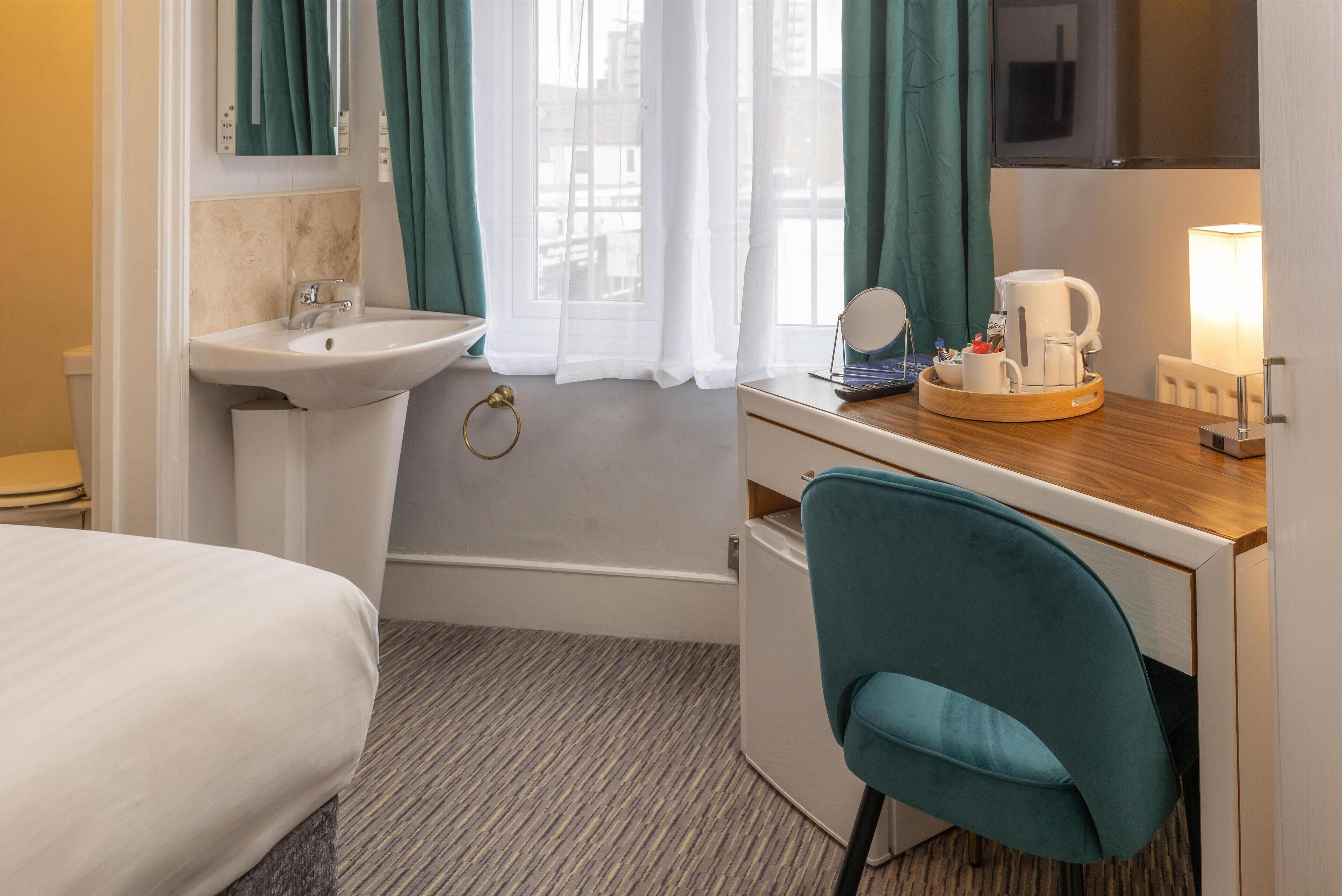 A hotel room with a bed, a sink, a bathtub, a desk with a chair, and a window with curtains.