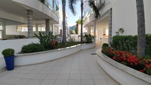 A modern hotel corridor with a tiled floor, indoor plants, and a view of the surrounding buildings. - Porto Del Mar - Canasvieiras (Florianópolis)