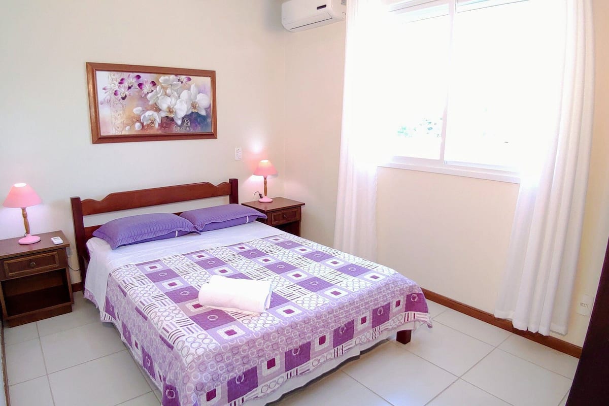 A neatly made bed with a patterned bedspread, two bedside lamps, a nightstand, and a wall-mounted picture.