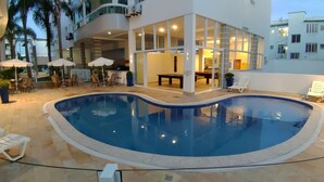 An indoor swimming pool with a curved edge, surrounded by lounge chairs and umbrellas. - Porto Del Mar - Canasvieiras (Florianópolis)