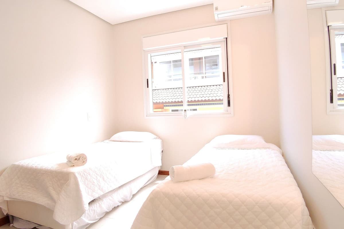 A room with two beds, a window, and an air conditioning unit.