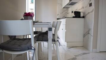 Uma cozinha moderna com armários brancos, uma moldura de backsplash em mármore e uma área de jantar com uma cadeira branca e assento acolchoado.