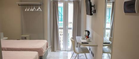 Quarto de hotel com duas camas, uma escrivaninha com cadeira, televisão e varanda com vista.