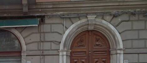 Un edificio con una puerta doble de madera grande y ornamentada, un persiano metálico cerrado y un balcón con barandillas de metal decorativas.