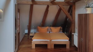 A loft bedroom with exposed wooden beams, a wooden bed with orange bedding, and a potted plant on the wall. - Altstadt Pension Potsdam (Potsdam)