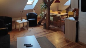 A loft-style room with exposed wooden beams, a skylight, a dining area with yellow chairs, a black chair, a small table with a vase, and a remote control on the table. - Altstadt Pension Potsdam (Potsdam)