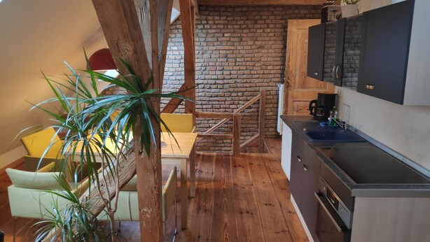 A cozy kitchen with wooden floors, a brick wall, and a staircase leading to an upper level. - Altstadt Pension Potsdam (Potsdam)