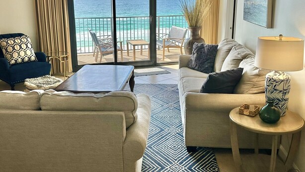 Una sala de estar con sofá, sillón y mesa de centro, una lámpara y vista al océano a través de amplios ventanales corredizos.