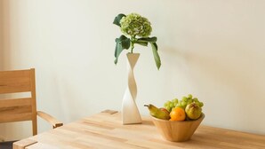 Una mesa de comedor de madera con un jarrón blanco y un frutero.