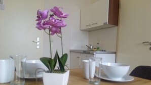 Una mesa de comedor con un jarrón blanco con flores moradas, platos blancos y vasos transparentes.