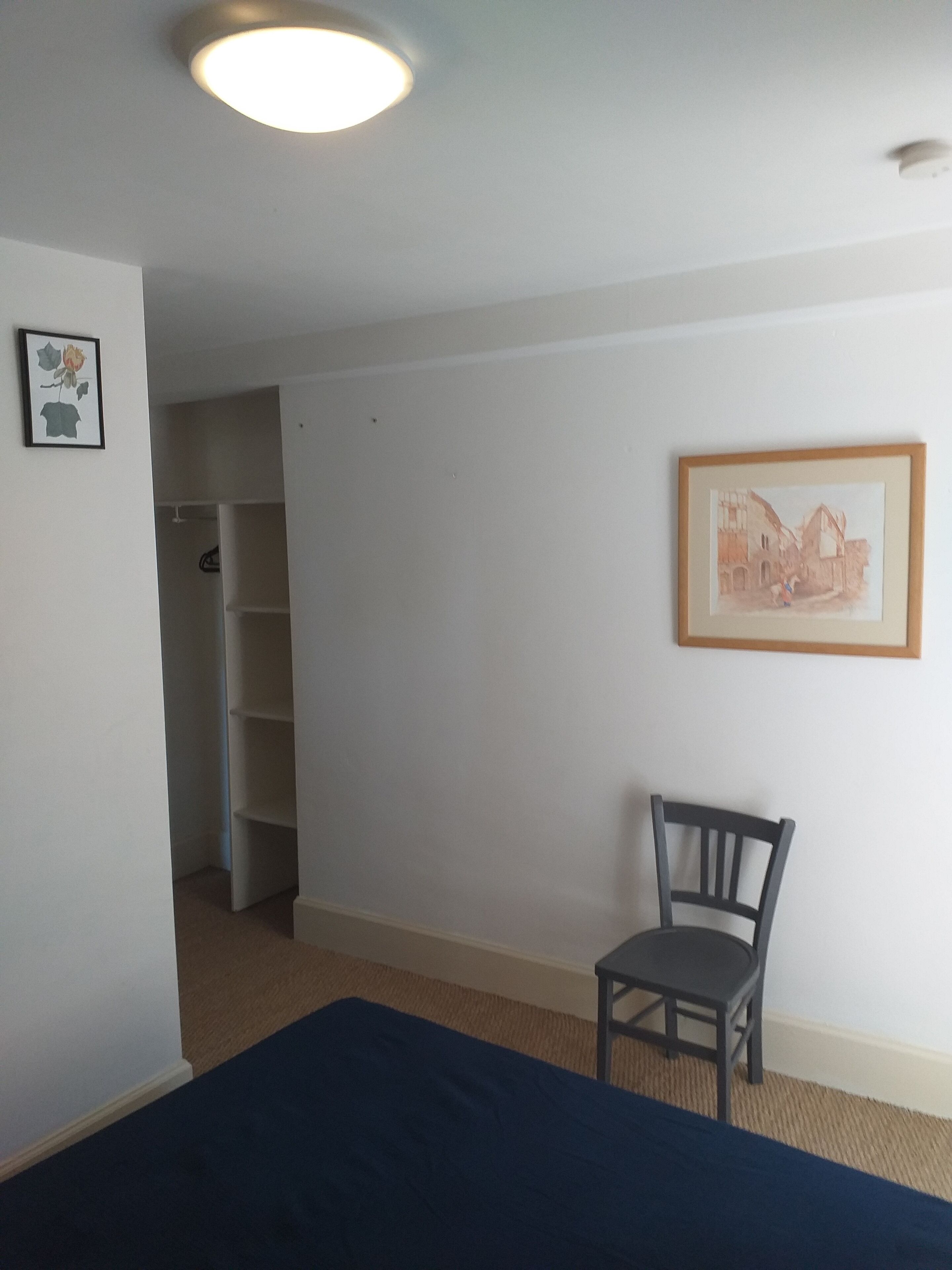 Une chambre à coucher avec un lit, une chaise, une armoire et un tableau au mur.