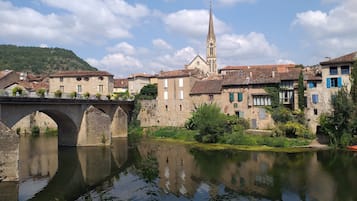 A stone bridge over a calm river, reflecting the surrounding buildings and a church with a tall spire.