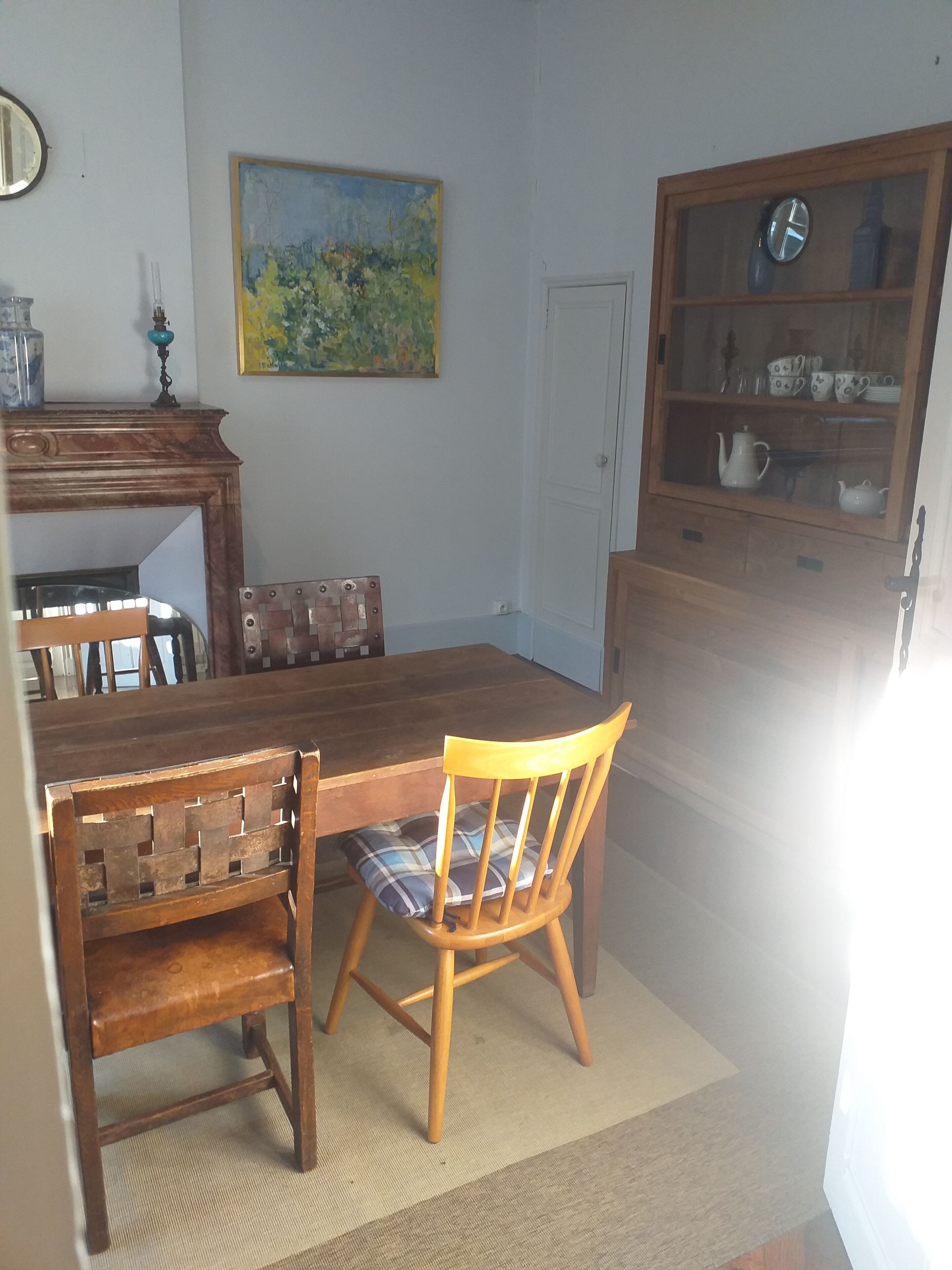 Un coin repas avec une table en bois, deux chaises, un tableau accroché au mur et un meuble avec des portes en verre.