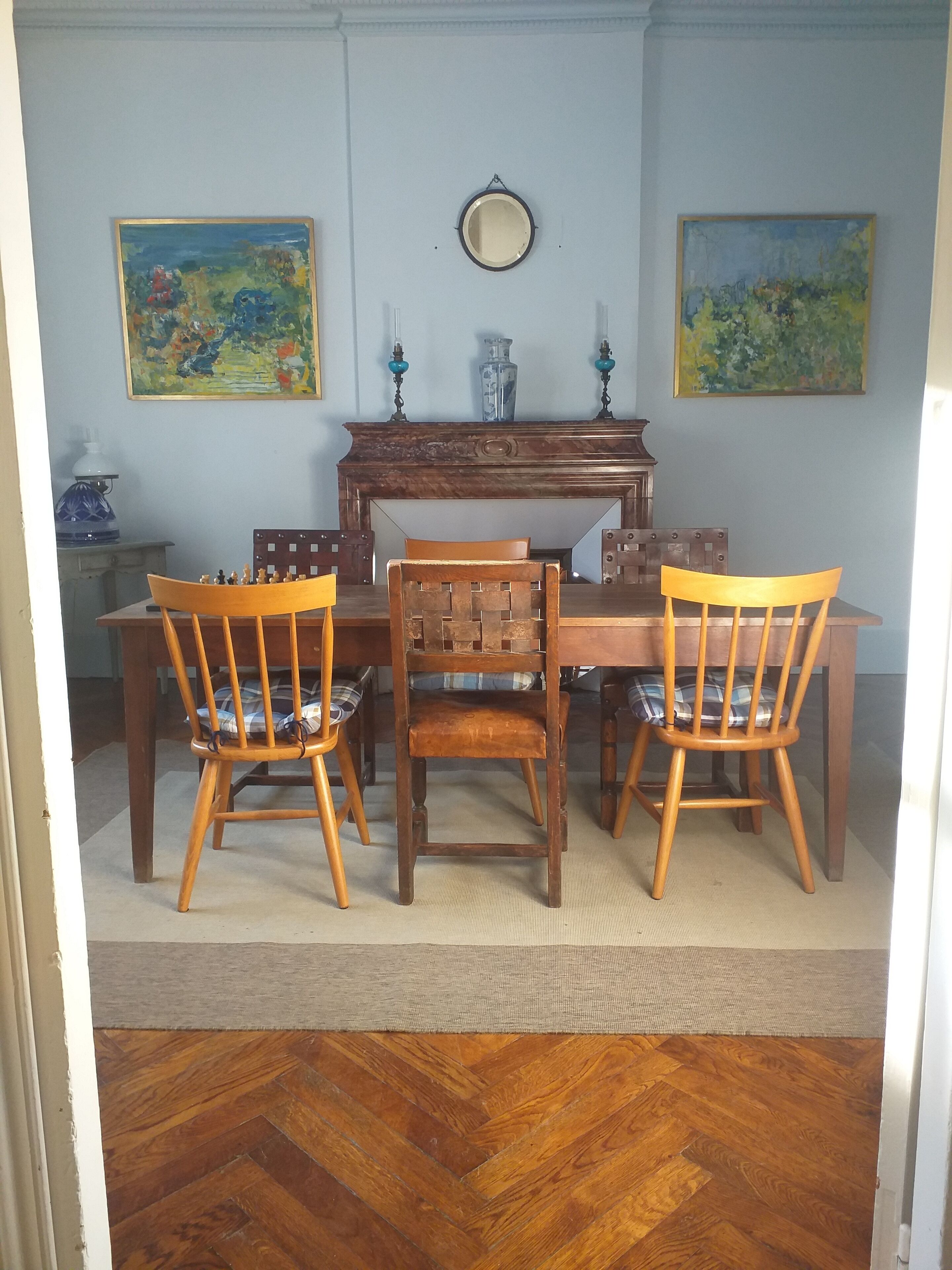 A dining area with a wooden table and chairs, a decorative mirror, and two paintings on the wall.