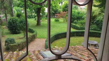 Vista de un jardín a través de una reja metálica, con un camino de piedra y abundante vegetación.