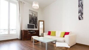 A living room with a white sofa, a glass coffee table, a wooden entertainment unit, and a large window. - Rue d'Antibes: modern apartment ! (Cannes)