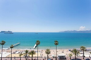 A beach with palm trees, a pier, and a cruise ship in the distance.