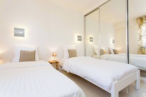 A hotel room with two beds, a large mirror, bedside lamps, and a wardrobe.