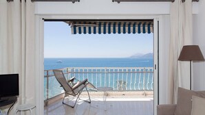 Un balcón con vista al mar, un sofá, un televisor y una lámpara.