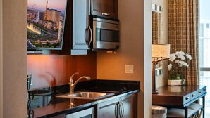 A modern kitchen with a stainless steel microwave, a built-in oven, a double sink, and a flat-screen TV mounted above the counter. - Luxury StripView 2-King Suites+No Resort Fee+Pool (Las Vegas)