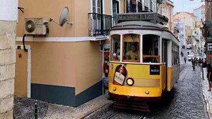 A yellow tram with the number 541 on a cobblestone street, passing by a building with a balcony and a satellite dish. - Tram & Fado Memory House (Lisbon)