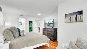A modern bedroom with a large bed, a dresser, a television, and artwork on the walls. - 314 C Shipwatch by AvantStay | OCEANFRONT WITH OCEAN VIEW (Isle Of Palms)