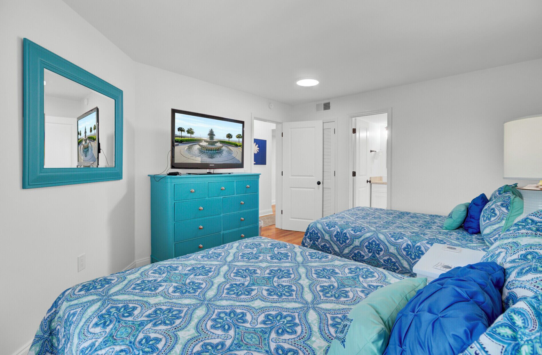 A bedroom with two beds, a dresser, a mirror, and a TV.