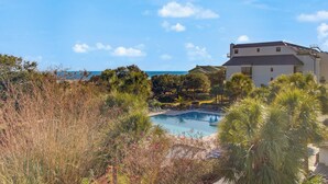 A pool surrounded by lush greenery and a white building with a view of the ocean. - 314 C Shipwatch by AvantStay | OCEANFRONT WITH OCEAN VIEW (Isle Of Palms)