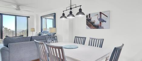 Un comedor con una mesa blanca y sillas grises, un sofá gris y un ventilador de techo.