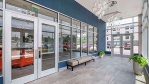 A modern building entrance with glass doors, a bench, and potted plants. - Cambria Hotel Nashville Airport (Nashville)