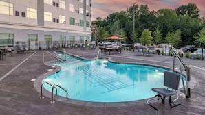 A swimming pool with a curved design, surrounded by a paved deck and a fence. - Cambria Hotel Nashville Airport (Nashville)