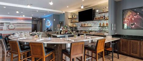 Un área de bar moderna con una isla central, taburetes y una variedad de botellas y vasos.