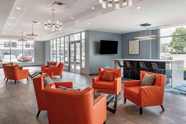 Un vestíbulo moderno con sillas naranjas, una recepción y grandes ventanales que ofrecen vistas al exterior.