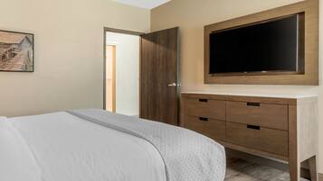 A bedroom with a bed, a wooden wardrobe, a television mounted above it, and a painting on the wall.