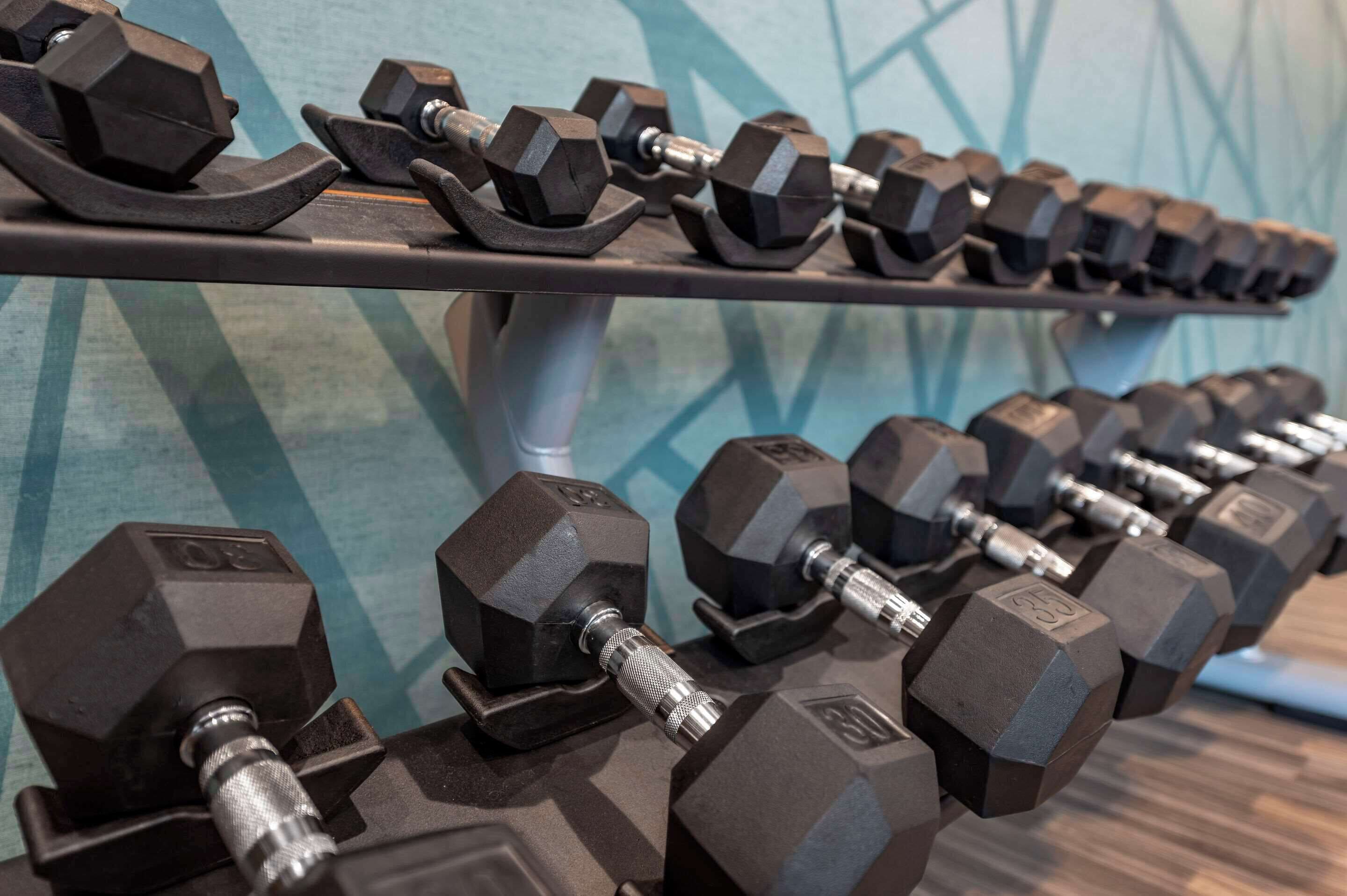 A rack of hexagonal dumbbells with weight markings, arranged on a shelf against a geometric patterned wall.